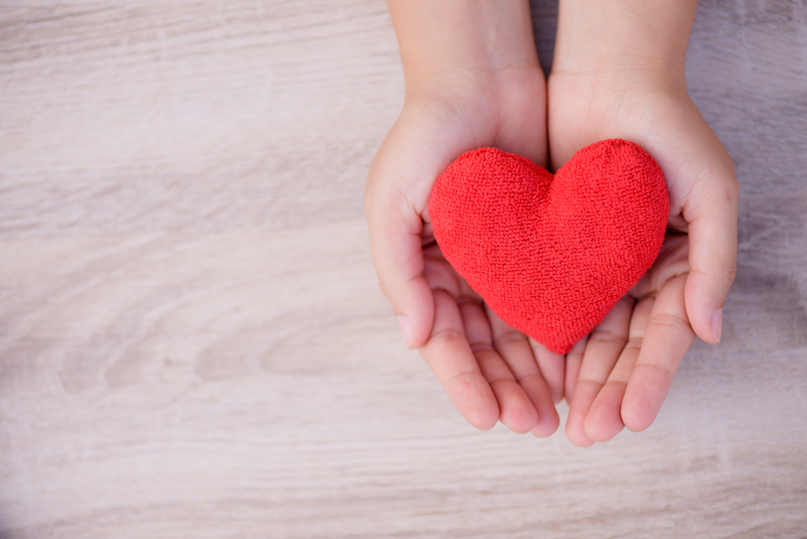 Health care, love, organ donation, family insurance and CSR concept. adult and child hands holding handmade red heart on wooden background.